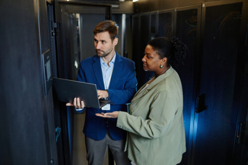 Two business professionals in a server room discuss data storage options